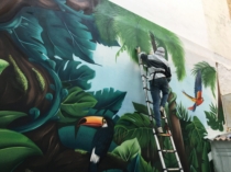Artista pintando un tucán en el mural tropical exterior