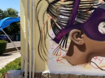 Detalle del proceso de graffiti de una superheroína en una fachada escolar