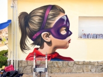 Niña con máscara de superheroína pintada en una fachada escolar
